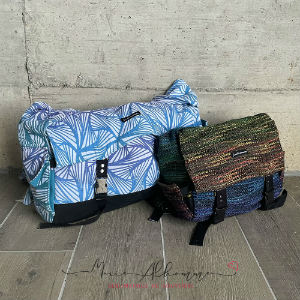 Two babywearing bags next to each other, the big one is blue while the other is a dark rainbow